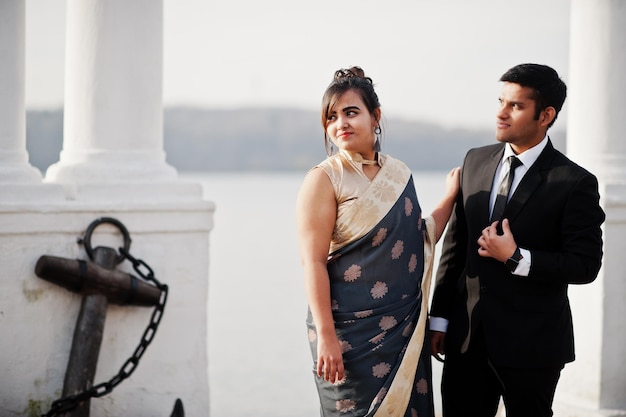 Couple d'amis indiens élégants et à la mode de femme en sari et homme en costume posé sur le rivage de la marina