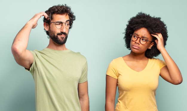 Photo couple d'amis multiracial se sentant perplexe et confus, se grattant la tête et regardant sur le côté