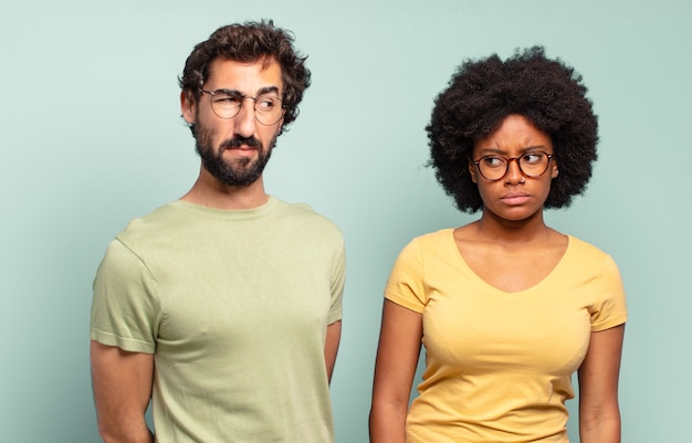 Couple d'amis multiraciaux se sentant triste, bouleversé ou en colère et regardant de côté avec une attitude négative, fronçant les sourcils en désaccord