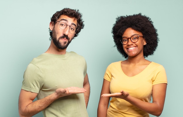 Photo couple d'amis multiraciaux souriant joyeusement, se sentant heureux et montrant un concept dans l'espace de copie avec la paume de la main