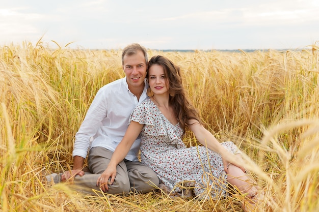 Couple d'amour heureux assis dans le blé sur le terrain. Homme et femme sur la prairie d'été