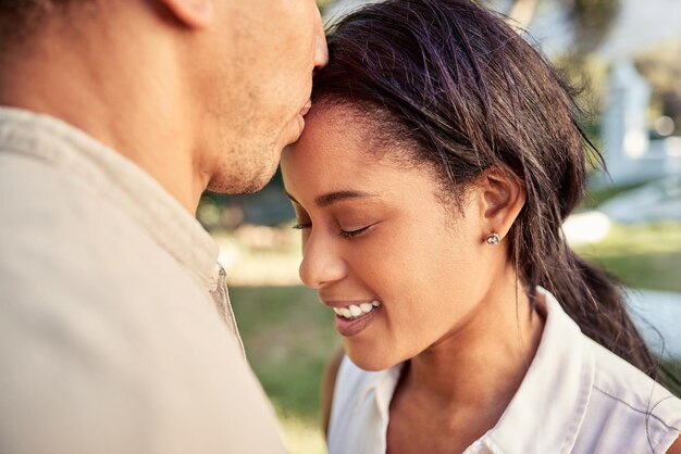 Couple amour et parc extérieur pour créer des liens avec un baiser sur le front montrant l'engagement, la confiance et le soutien avec un sourire Bonheur, soins et nature avec un jeune homme et une femme dans une relation amoureuse