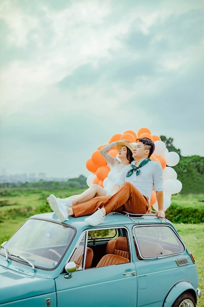 couple d&#39;amoureux assis au sommet de la voiture avec des ballons colorés