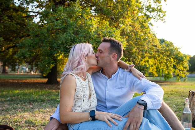 Couple d'amoureux assis sur l'herbe dans le parc s'embrasse passionnément sur la bouche