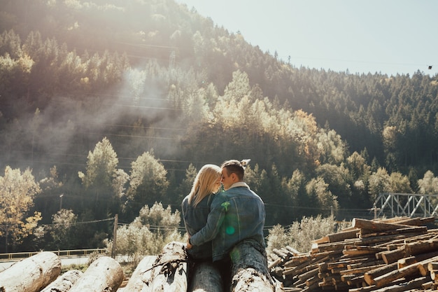 Un couple amoureux assis sur la pile de bois de chauffage dans la belle forêt d'automne colorée.