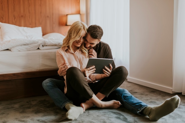 Couple d&#39;amoureux assis sur le sol dans la chambre et en utilisant une tablette numérique