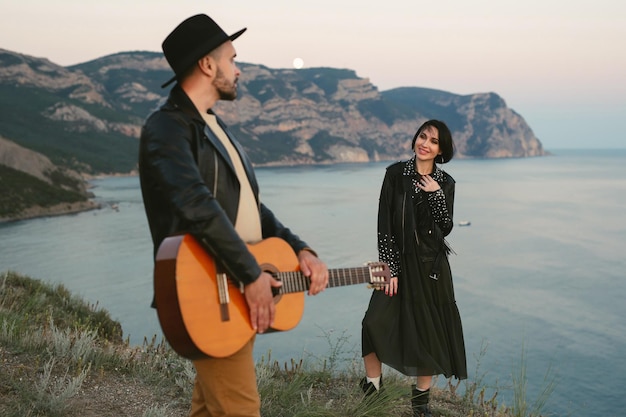 Couple amoureux au sommet d'une montagne surplombant la mer Un homme au chapeau joue de la guitare