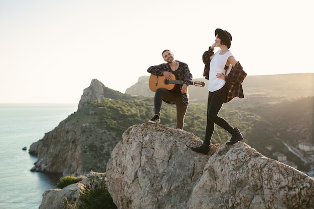 Couple amoureux au sommet d'une montagne surplombant la mer L'homme joue de la guitare une femme danse et chante