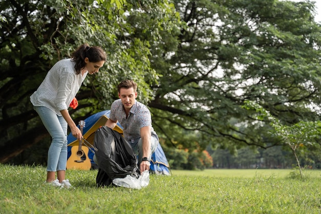 Couple d'amoureux bénévoles portant des gants marchant pour ramasser les ordures dans le parc Pour garder l'environnement propre