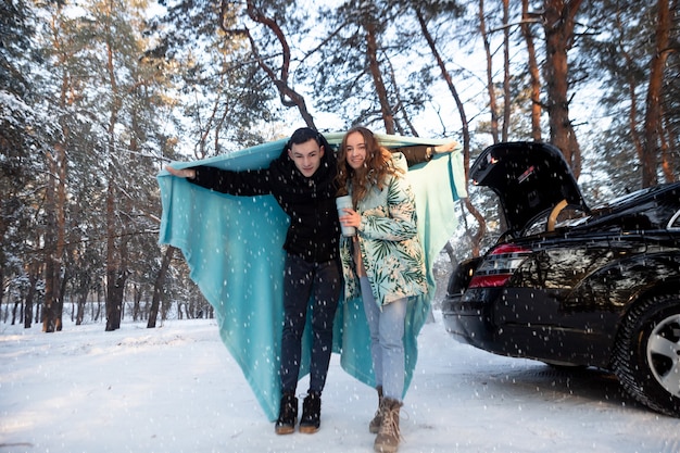 Un couple d'amoureux boit du thé dans un thermos sur fond de forêt d'hiver enneigée