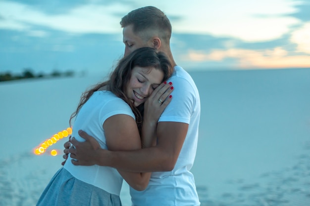 Couple amoureux câlins romantiques dans le désert de sable. Soirée, ambiance romantique, dans le sable brûler des bougies.