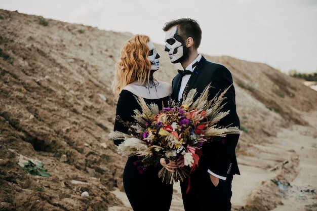 Photo un couple amoureux célèbre halloween en costumes et en maquillage avec un bouquet de fleurs séchées