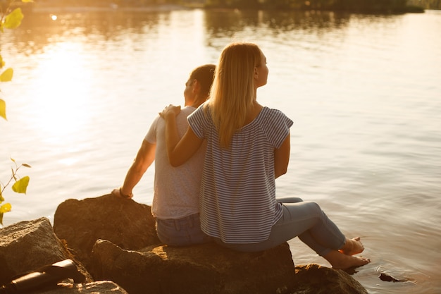 Photo couple amoureux sur une côte rocheuse à sunet en soirée d'été. concept histoire d'amour en plein air. week-end en famille dans la nature. famille heureuse au repos à l'extérieur. émotionnel homme et femme étreintes et baisers