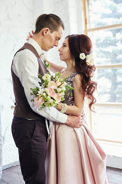 Couple amoureux dans de beaux vêtements et un gros bouquet de fleurs près d'une grande fenêtre. Histoire d'amour