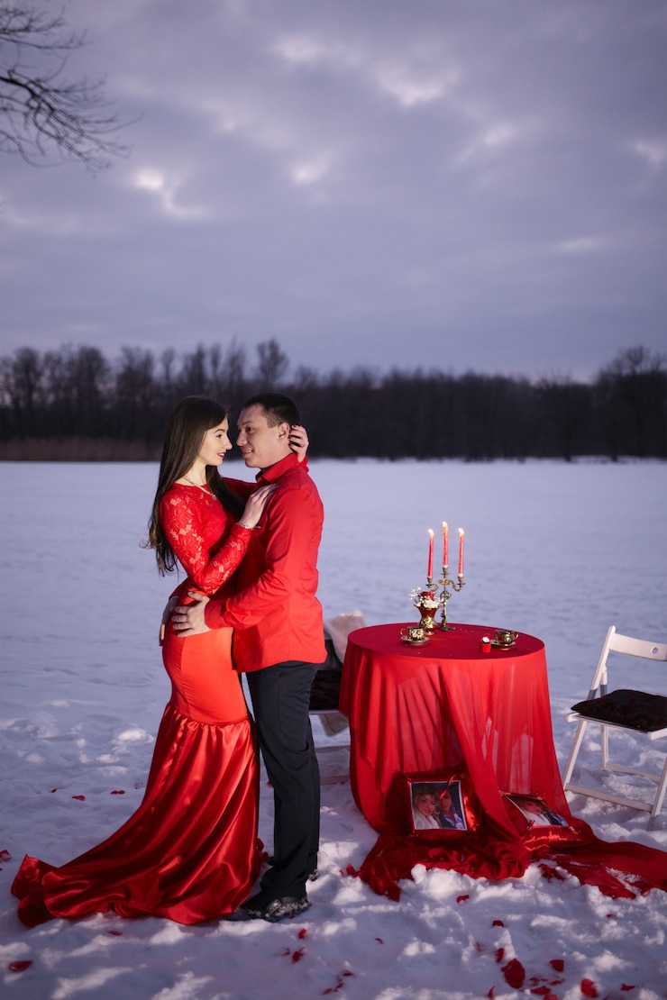 Photo couple d'amoureux dans de beaux vêtements rouges sur le stand de rue près de la table avec fond de neige d'hiver