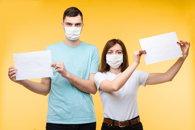 Couple amoureux dans des masques médicaux blancs ont peur du coronavirus et montre des affiches