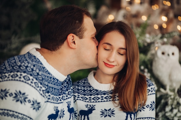 Couple amoureux dans des pulls confortables avec impression de Noël s'embrassant ensemble