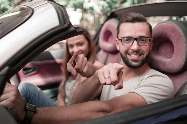 Couple d'amoureux dans une voiture décapotable pointant vers vous