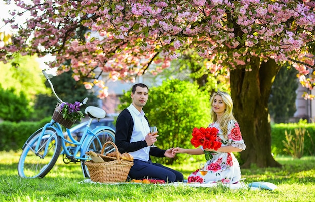 Couple amoureux date de pique-nique Week-end de printemps Pique-nique romantique avec du vin Fleurs symbole de romance et d'affection Profiter de leur rendez-vous parfait Couple se détendre dans le parc avec vélo Heureux ensemble