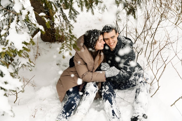 Couple d'amoureux en doudoune lors d'une promenade hivernale. Homme et femme s'amusant dans la forêt givrée. Rendez-vous romantique en hiver. Ambiance de Noël d'une jeune famille. Histoire d'amour d'hiver