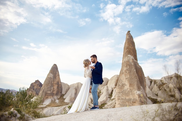 Couple amoureux embrasse et embrasse dans de fabuleuses montagnes dans la nature. Fille en robe longue blanche avec bouquet de fleurs dans les mains, homme en veste. Mariage dans la nature, les relations et l'amour