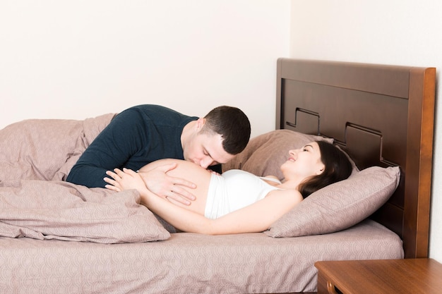 Un couple amoureux et enceinte s'embrasse sur le lit le matin.