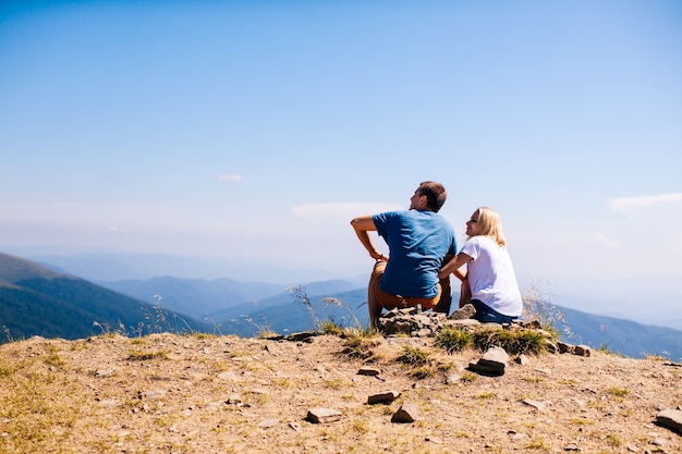 Un couple d'amoureux est assis sur une colline et admire la vue sur les montagnes