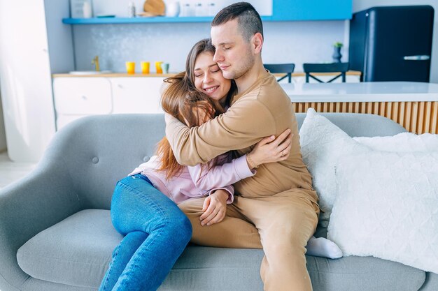 Un couple amoureux est assis à la maison sur le canapé de la cuisine, serrant dans ses bras, ils sont heureux ensemble