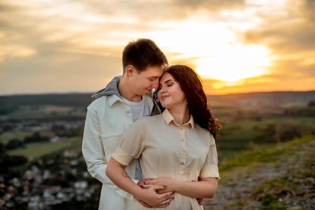 Un couple amoureux, un gars et une fille se tiennent sur une montagne au coucher du soleil, s'embrassent et s'embrassent