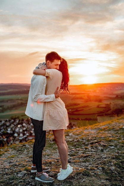 Un couple amoureux, un gars et une fille se tiennent sur une montagne au coucher du soleil, s'embrassent et s'embrassent