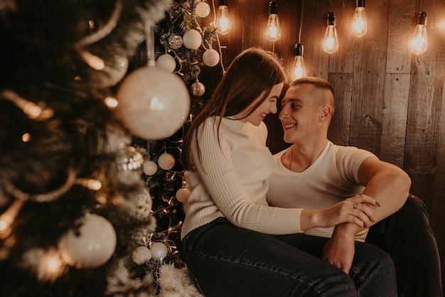 Couple amoureux gars et fille sont étreignant s'embrasser près de l'arbre de Noël près d'une fenêtre