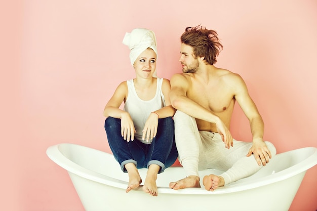 Couple amoureux d'un homme et d'une femme musclés avec une serviette assis sur une baignoire blanche sur fond rose, famille, relation et romance, spa et beauté, détente et hygiène, soins de santé