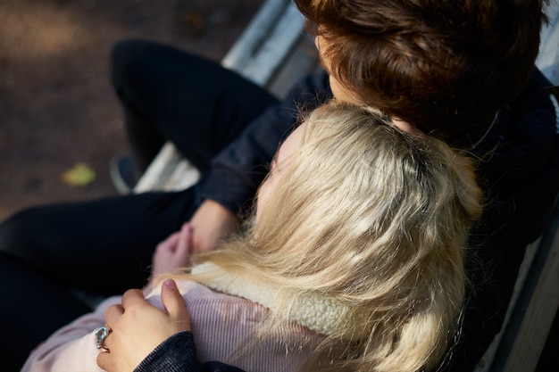 Couple d'amoureux des hommes et des femmes assis sur un banc, se reposant dans les rayons du soleil d'automne