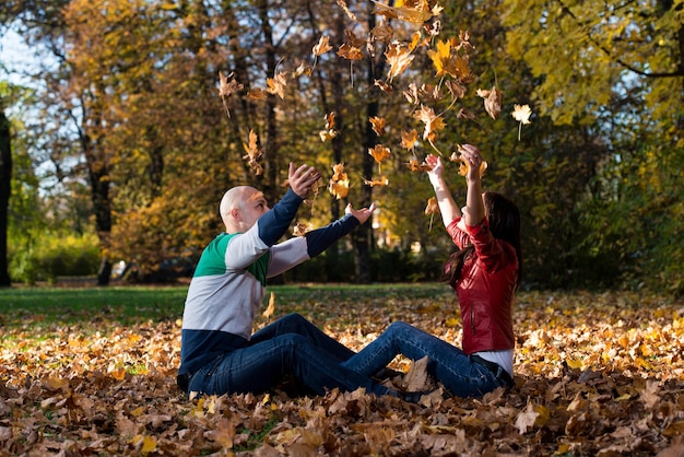 Couple d'amoureux jeter les feuilles dans le parc d'automne