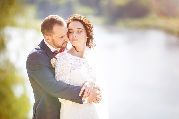 Un couple d'amoureux de jeunes mariés se promène près d'une large rivière en journée ensoleillée d'été