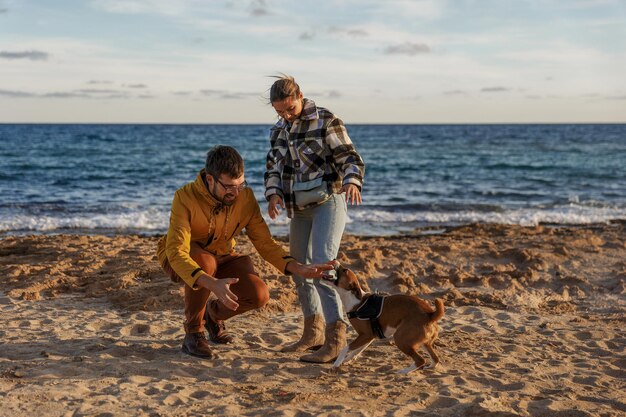 Un couple d'amoureux joue avec leur chien à la plage, les gens de race blanche, les gens, le mode de vie animal et le concept de la nature