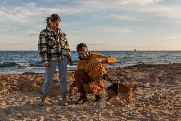 Un couple d'amoureux joue avec leur chien à la plage, les gens de race blanche, les gens, le mode de vie animal et le concept de la nature