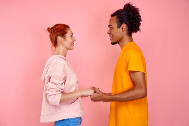 Couple d'amoureux joyeux gingembre femme et homme afro-américain se tenant la main et se regardant