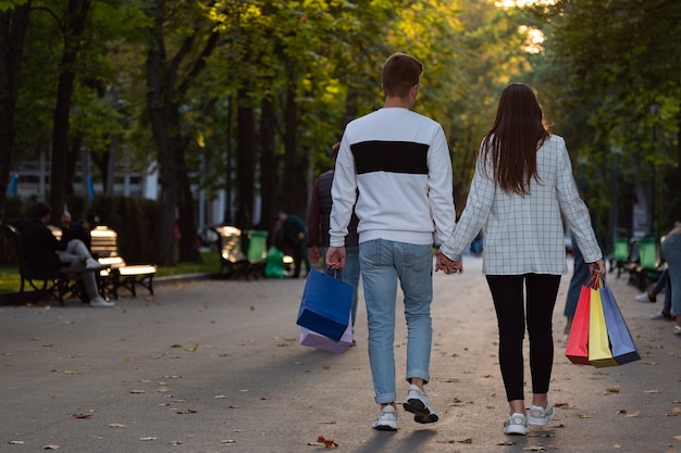 Couple amoureux marchant dans le parc avec des sacs à provisions. Vue arrière.