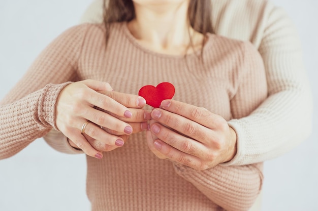 Couple amoureux méconnaissable s'embrassant tout en tenant un petit coeur rouge dans leurs mains