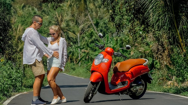 Couple d'amoureux sur une moto rouge en vêtements blancs lunettes de soleil sur le sentier de la route forestière Dancing road