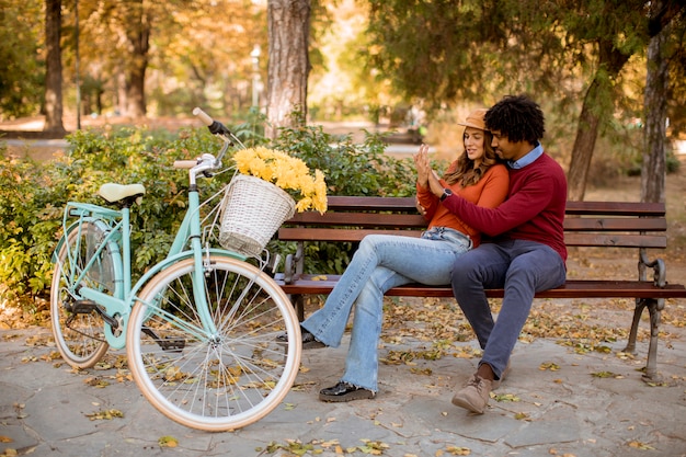 Couple d'amoureux multiratial assis sur un banc dans le parc de la ville en automne