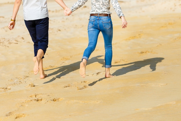 Couple amoureux pieds nus traversant la plage de sable