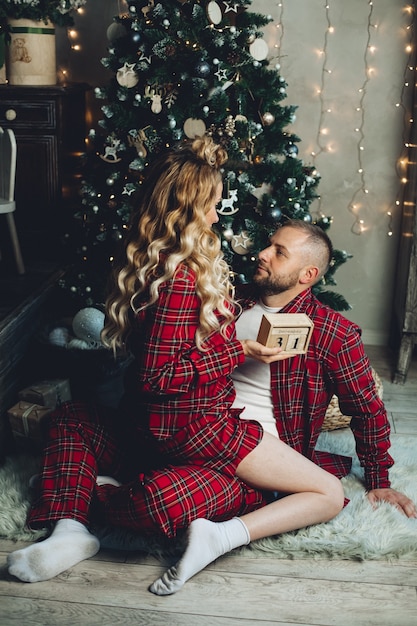 Couple amoureux portant des pyjamas assortis alors qu'il était assis sur le sol près de l'arbre de Noël à la maison