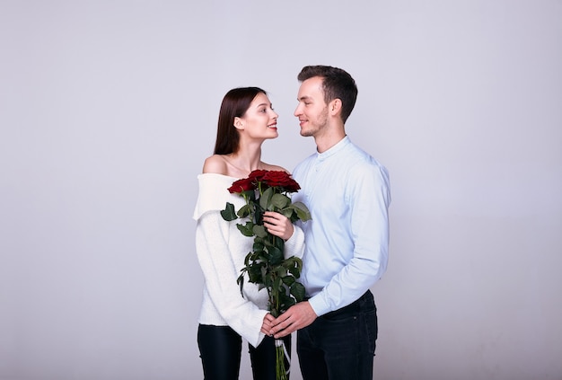 un couple d'amoureux posant sur un fond blanc avec un bouquet de roses rouges.