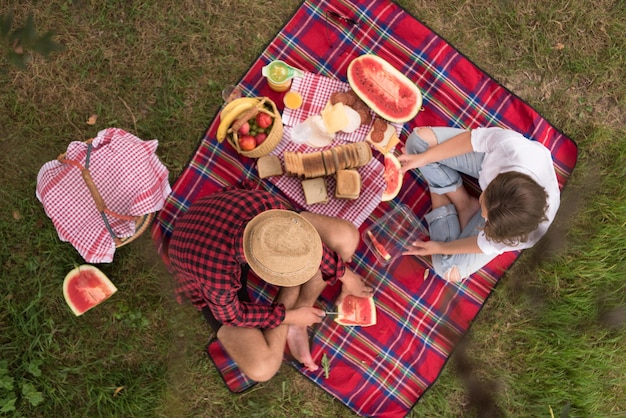 Photo couple amoureux profitant de l'heure du pique-nique boire et manger dans la belle nature sur la vue de dessus de la rive du fleuve