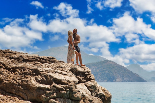 Couple d'amoureux profitant d'une lune de miel sur un rocher avec vue de luxe marchant montrant l'émotion sur fond de mer azur