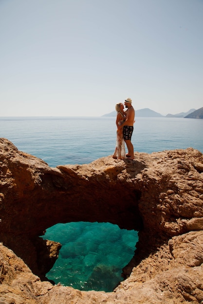 Couple d'amoureux profitant d'une lune de miel sur un rocher avec vue de luxe marchant montrant l'émotion sur la mer d'azur