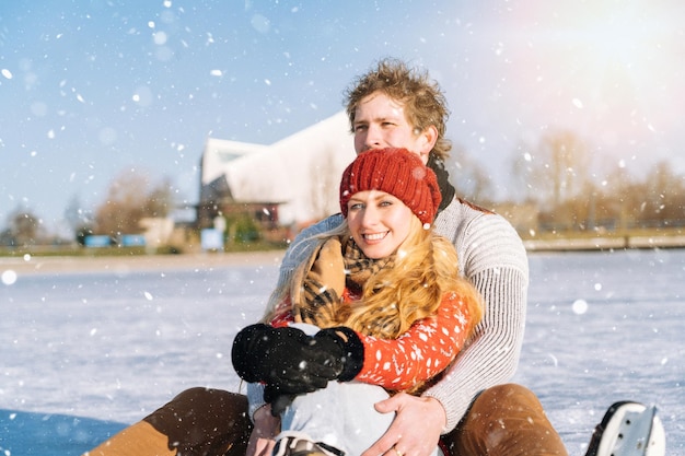 Couple d'amoureux en pulls chauds s'amusant sur la glace femme et homme patin à glace à l'extérieur sous le soleil de neige