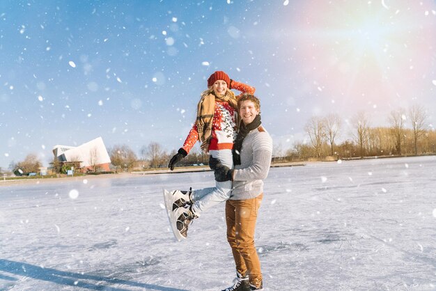 Couple d'amoureux en pulls chauds s'amusant sur la glace femme et homme patin à glace à l'extérieur sous le soleil de neige